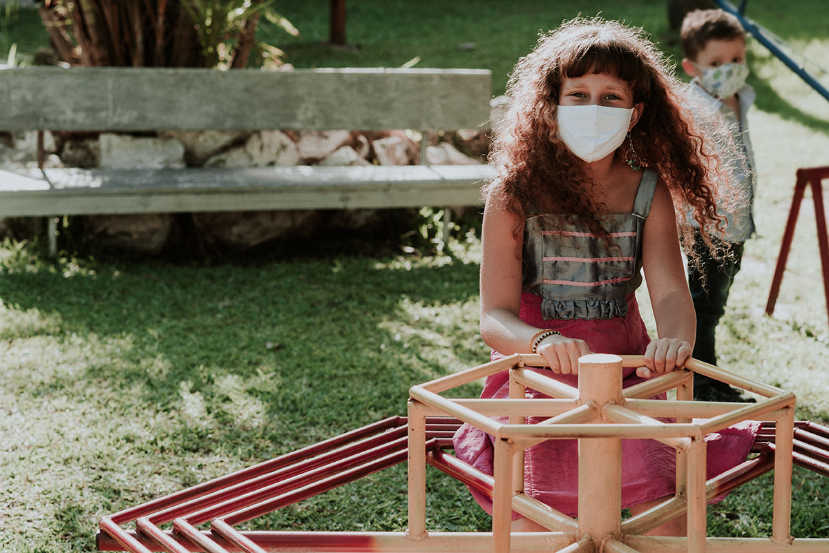 A young girl plays one the playground while wearing a mask